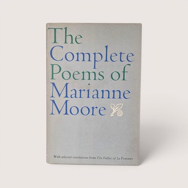 A vintage 1967 hardcover edition of The Complete Poems of Marianne Moore with blue and green typography on a gray dust jacket.
