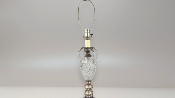 A tall vintage table lamp with a diamond-cut crystal body and glass prisms hanging from the top. It features a decorative silver-colored metal base and a brass-toned harp.