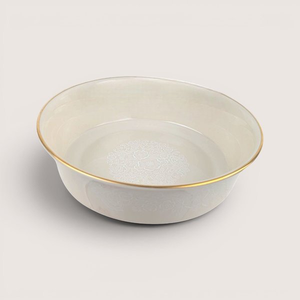Round ceramic serving bowl with a white floral medallion design on the interior and a gold rim, centered on a plain linen background.