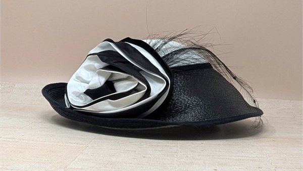 A vintage black and white woven straw hat. It features a crisp white crown and a wide black brim, accented by a large, voluminous fabric rosette in matching black and white tones.