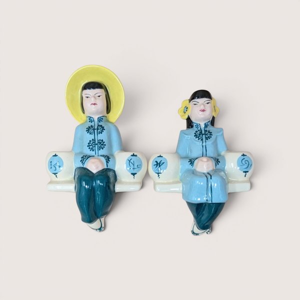 Pair of ceramic Asian-inspired shelf sitter figurines wearing light blue and teal attire, centered on a plain linen background.