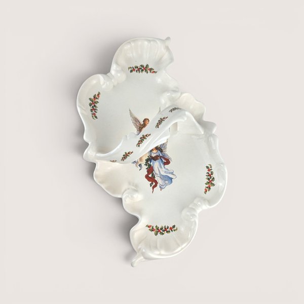 White ceramic divided serving dish with an integrated center handle, featuring an illustration of an angel holding a book surrounded by holly leaf accents, centered on a plain linen background.