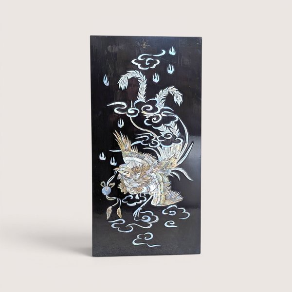 Vintage Asian black lacquer wood wall panel with iridescent mother of pearl inlay depicting a phoenix among clouds on a linen background