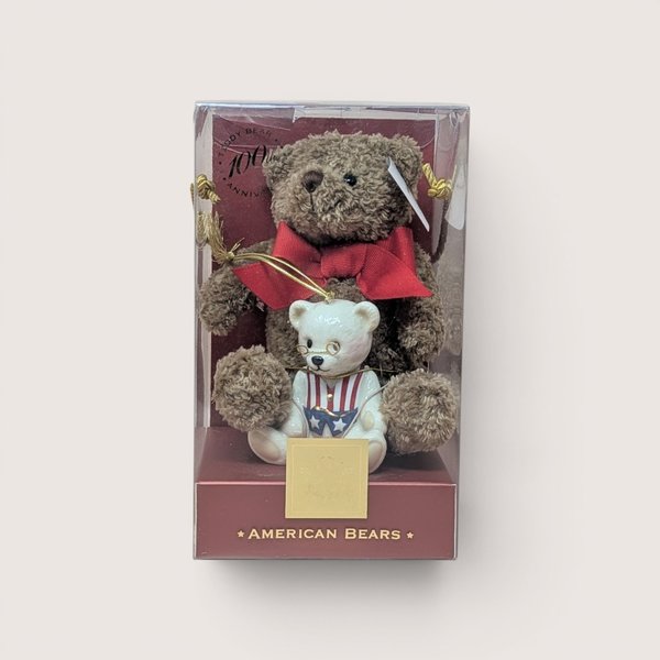 Boxed collector's set titled "AMERICAN BEARS" celebrating the Teddy Bear 100th Anniversary, containing a small brown plush teddy bear wearing a large red bow paired with a white porcelain teddy bear figurine dressed in a patriotic red, white, and blue vest with wire-rimmed glasses, centered on a plain linen background.