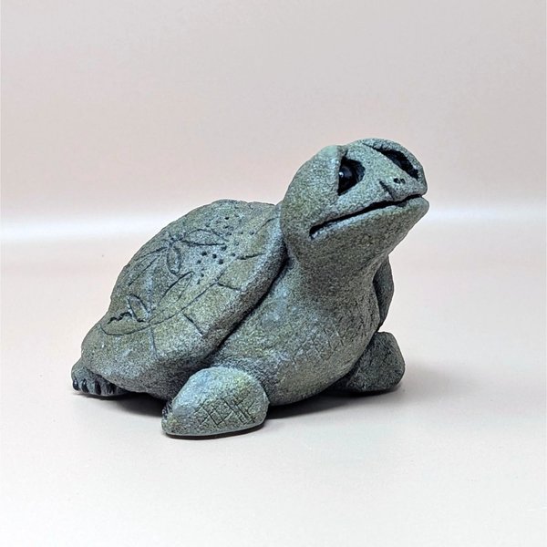 A 1993 Lou Ranken Slowpoke turtle figurine by Hallmark on a soft pink background. The highly textured gray resin sculpture shows a charming turtle looking upward with large expressive black eyes and a faintly etched leaf pattern on its shell.