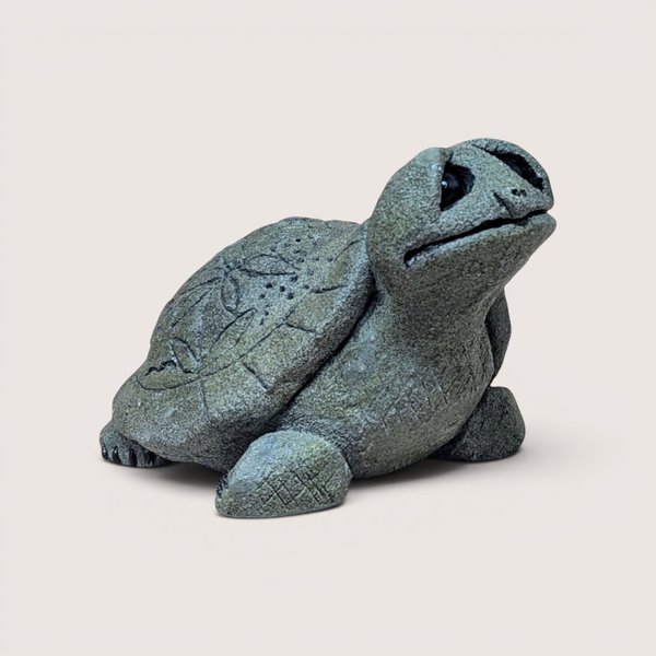 Vintage cast stone or resin turtle figurine with a textured, gray-green finish, featuring a stylized leaf pattern etched into its shell and its head tilted upward, centered on a plain linen background.