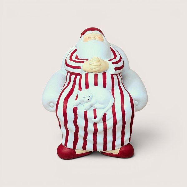 A vintage Department 56 Winter Silhouettes "Cat Nap" Santa figurine on a soft pink background. The matte white porcelain sculpture shows Santa sleeping soundly in a large armchair wearing red-striped pajamas with a white cat napping on his lap.
