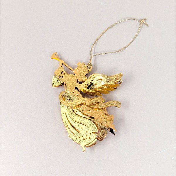 A 1999 Danbury Mint Millennium Angel Christmas ornament with its box on a soft pink background. The fine filigree brass angel is plated in gleaming 23kt gold, depicted in flight while blowing a long trumpet with a dated 1999 banner ribbon.