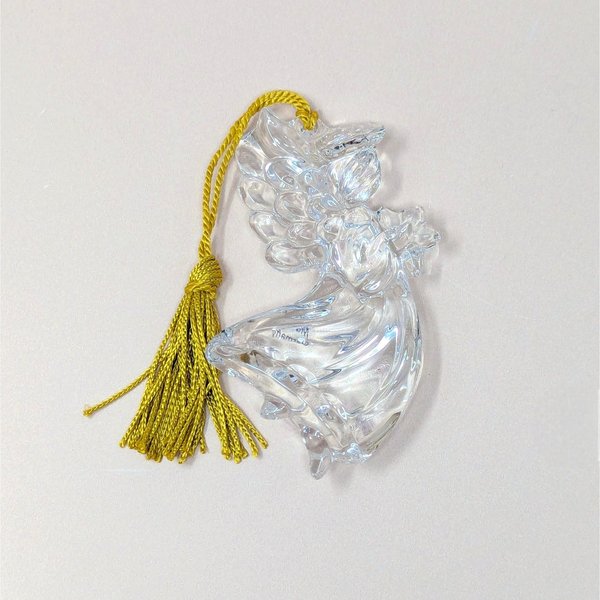A vintage Gorham crystal angel ornament with a gold tassel on a soft pink background. The fine German glass sculpture features a clear, faceted angel in flight holding a small star, catching the light with brilliant clarity.