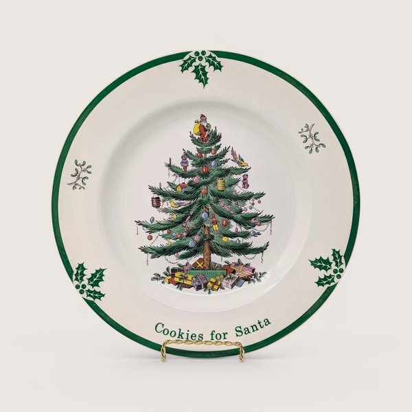 A round cream holiday plate featuring a central decorated Christmas tree design and green border on a plain background