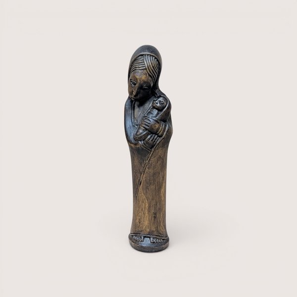 A slender hand carved wooden statue of Mary holding the infant Jesus on a plain background