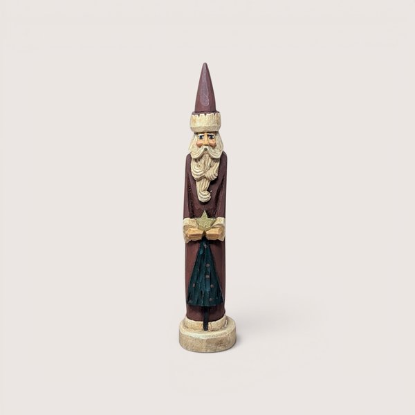 A tall, slender vintage hand-carved wooden Santa Claus figurine holding a gold star above a small green tree.