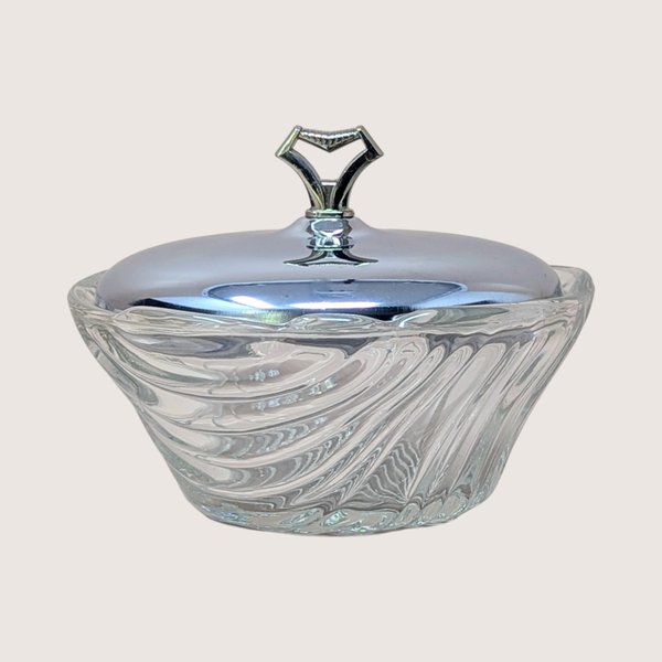 A vintage clear glass vanity bowl with a swirled pattern and a polished chrome lid featuring a geometric chevron handle.