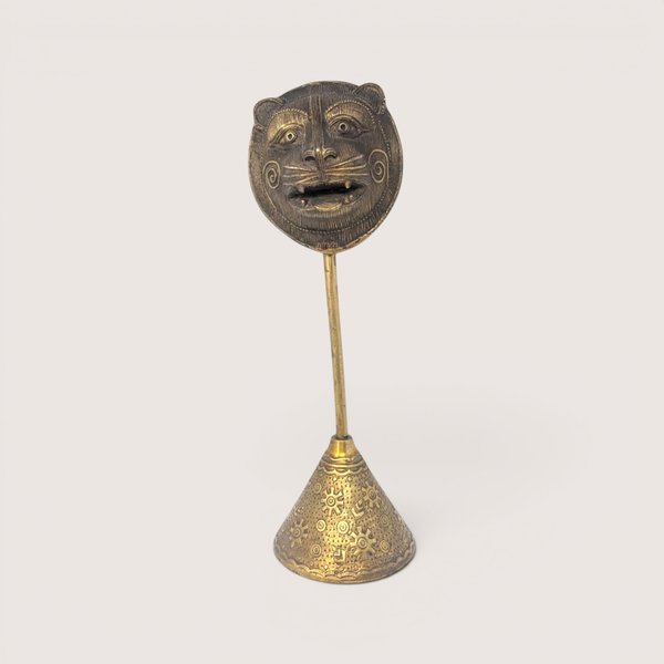 A vintage lost-wax cast brass tribal tiger mask sculpture mounted on a tall etched conical pedestal base.