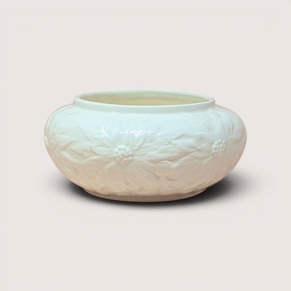 A round cream colored ceramic bowl with embossed poinsettia flowers resting on a light beige background