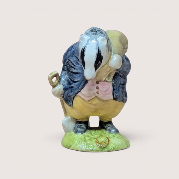A vintage porcelain badger figurine wearing a blue coat and yellow trousers holding a shovel on a plain background