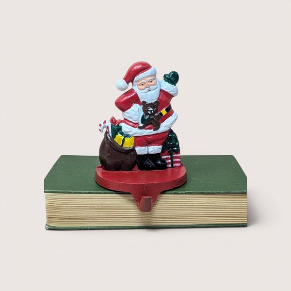 A vintage cast iron Santa Claus stocking holder with a toy sack sitting on a green book against a plain background