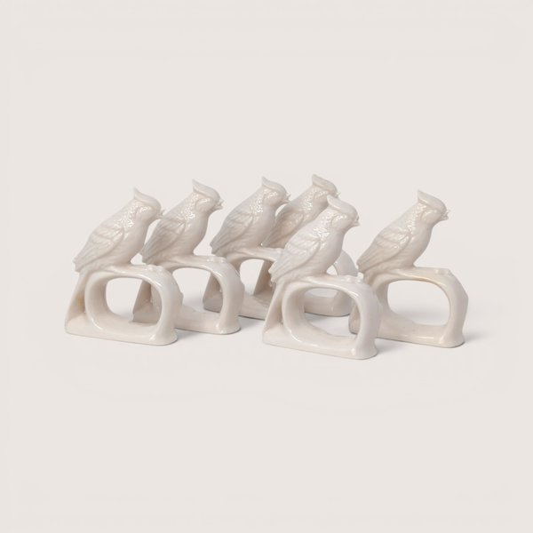 A set of vintage white porcelain napkin rings shaped like crested cardinal birds perched on branches on a plain background