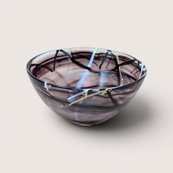 A vintage hand blown purple art glass bowl with abstract black white and yellow swirled lines on a beige background