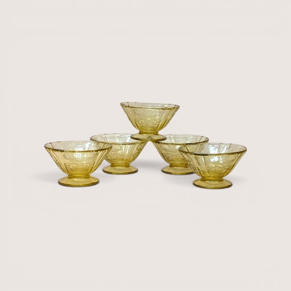Five amber depression glass sherbet cups stacked in a pyramid on a light beige backdrop