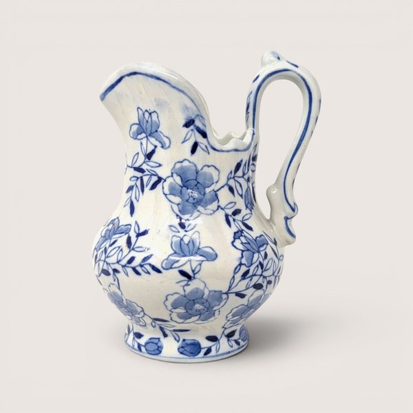 Hand painted blue and white floral ceramic pitcher with an elegant handle against a neutral background.