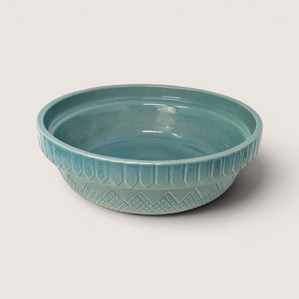 Teal blue glazed stoneware serving bowl with geometric embossed details along the outer rim on a solid background.