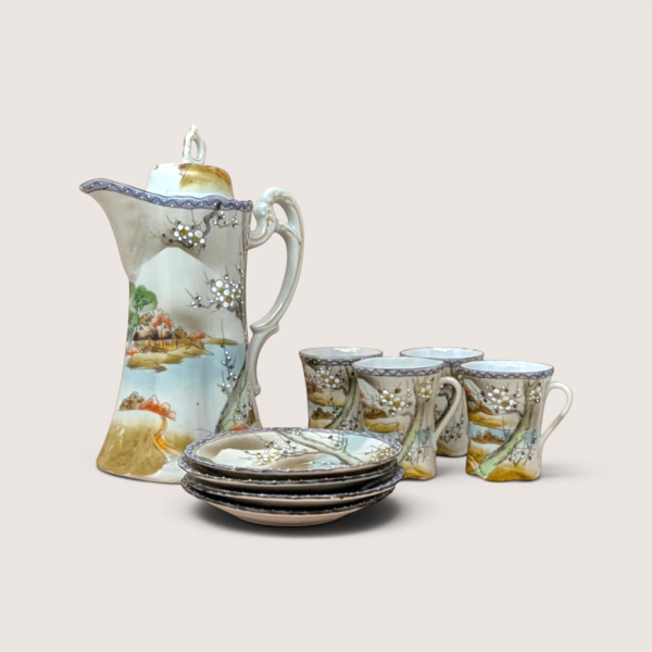Hand painted porcelain tea set with a tall teapot four cups and matching saucers featuring a scenic lake landscape on a solid background.