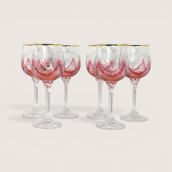 Six cut to clear cranberry wine glasses with frosted floral designs and gold rims on a solid background.
