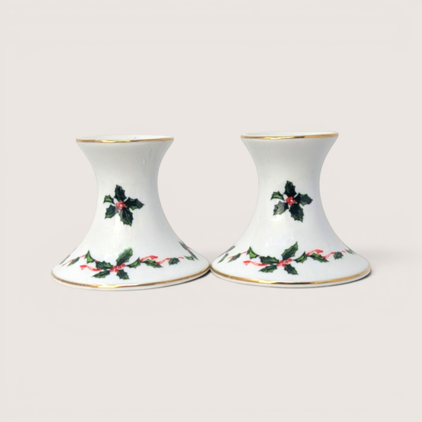Pair of white ceramic candlestick holders decorated with green holly leaves, red berries, and gold trim.