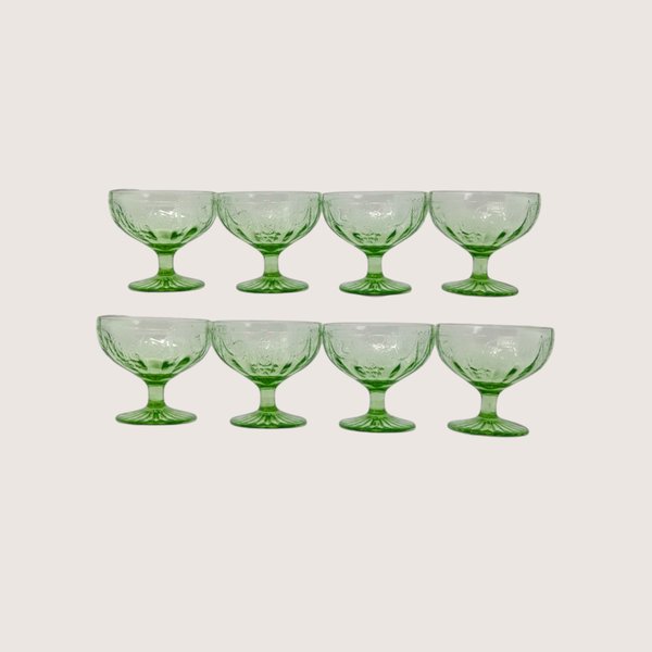 Eight green depression glass sherbet cups arranged in two rows of four against a plain off-white background