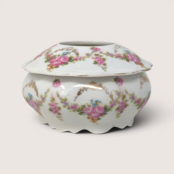 An antique porcelain hair receiver with pink floral swags and gold trim on a plain white background