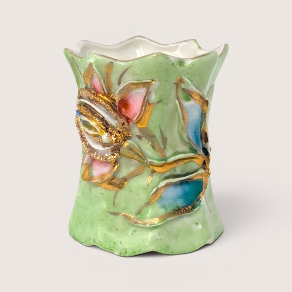A small light green ceramic toothpick holder with hand painted relief flowers and heavy gold gilding on a white background