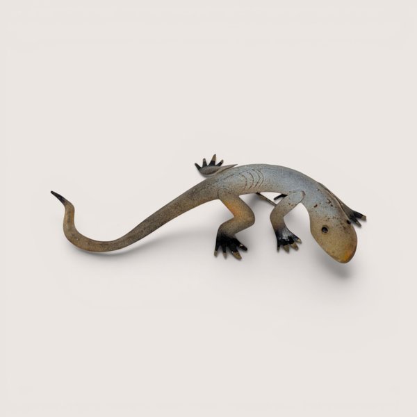 A small stylized metal lizard wall sculpture with a curved tail and mottled patina on a plain background