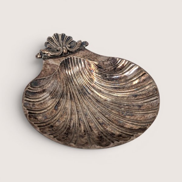 A vintage silver plated scallop shell shaped trinket dish with dark age tarnish on a plain white background