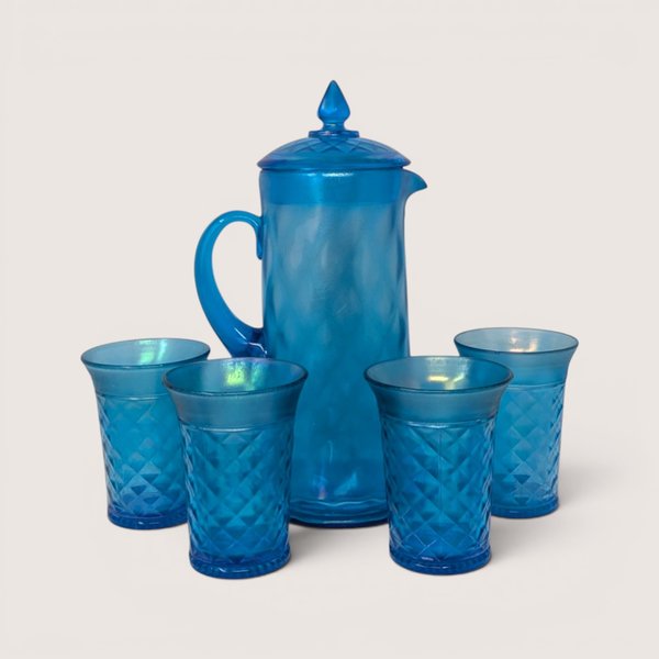 A vibrant celeste blue glass water pitcher with a matching lid surrounded by four diamond patterned tumblers