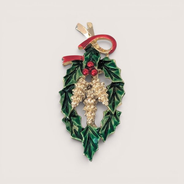 Vintage gold tone and enamel Christmas brooch featuring green holly leaves, red berries, and a red ribbon bow.
