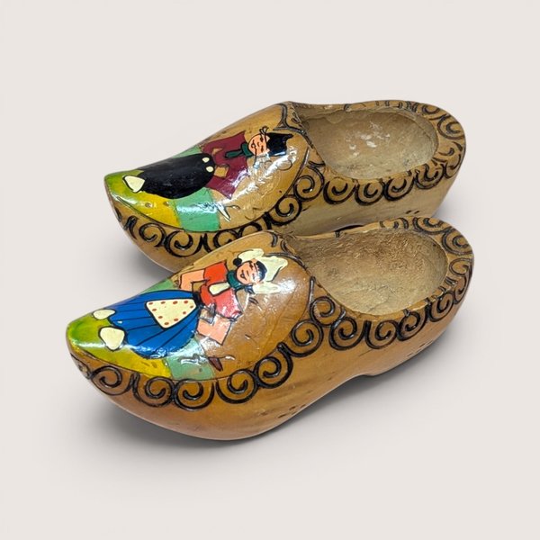 Pair of vintage hand-painted Dutch wooden clogs featuring traditional figures and carved swirl borders.