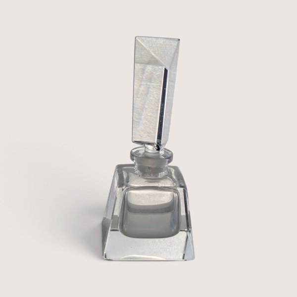 A vintage clear glass perfume bottle featuring a square base and a tall geometric frosted glass stopper against a neutral background.