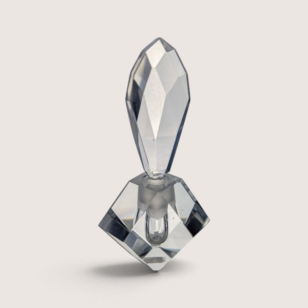 A vintage heavy cut crystal perfume bottle featuring a diamond-shaped base with a red foil label and a large multi-faceted teardrop stopper against a neutral background.
