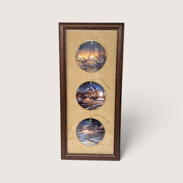 Vintage 1990s Terry Redlin set of three porcelain holiday ornaments featuring winter landscapes, professionally mounted in a wooden frame.