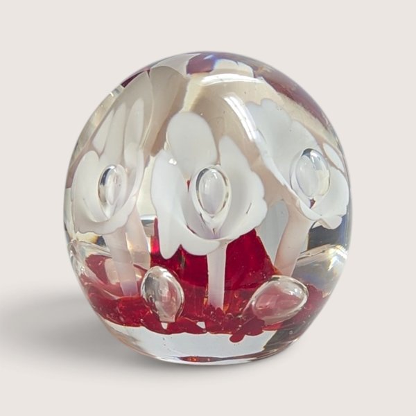 Vintage art glass paperweight featuring white flower motifs suspended over a vibrant red glass base.
