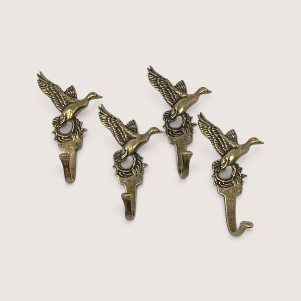 A set of four vintage metal wall hooks shaped like flying ducks with an antique brass finish arranged against a neutral background.