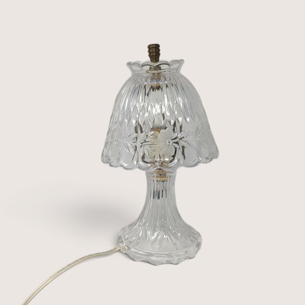 A small vintage clear cut glass boudoir lamp featuring a patterned shade with frosted floral details and a fluted base against a neutral background.