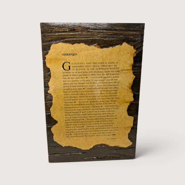 A vintage wooden wall plaque featuring the Desiderata poem printed on an aged parchment-style paper mounted onto a dark textured wood backing.