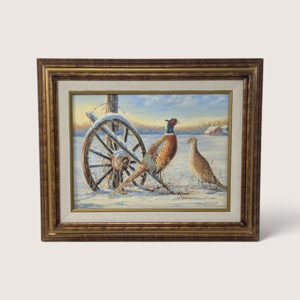 An original framed painting by Martha Spear depicting a rooster and hen pheasant standing in a snowy field beside an old wooden wagon wheel, set inside a textured wood frame with a fabric liner, showing the Fredrix canvas backing on the rear.
