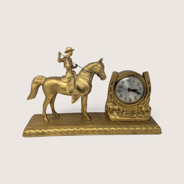 A vintage gold-tone metal western mantel clock featuring a cowboy on horseback next to a horseshoe clock face.