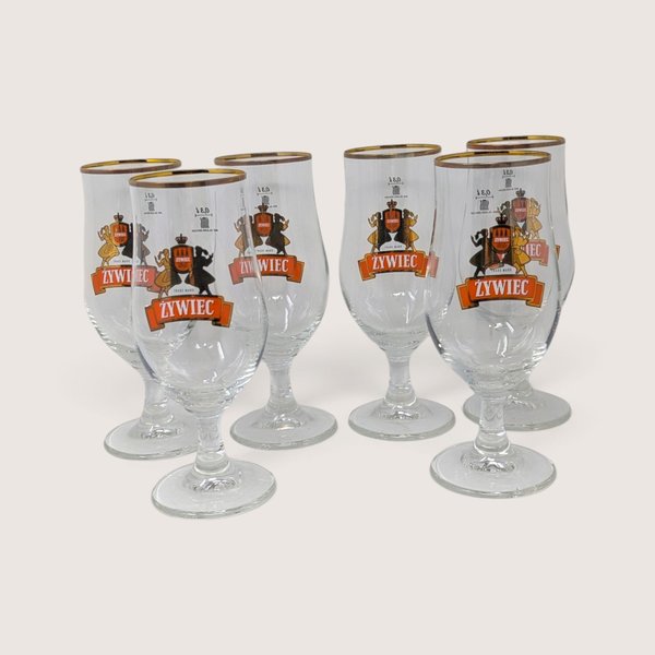 A set of six vintage Ritzenhoff Cristal Zywiec stemmed beer glasses with gold rims and folkloric graphics, displayed with their original packaging box.