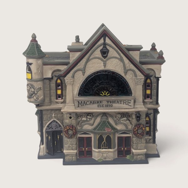 A vintage Department 56 Theater of the Macabre Halloween village building featuring gray stone details, skull carvings, double doors, and glowing windows.