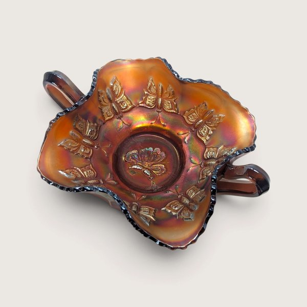 A vintage Fenton marigold carnival glass handled bon bon dish featuring an embossed butterfly pattern on a neutral background.