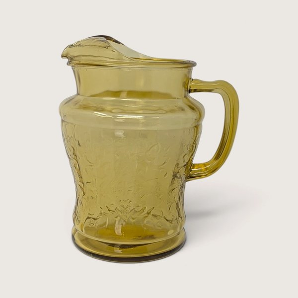 A vintage Federal Glass amber yellow depression glass pitcher featuring the Madrid scroll pattern on a neutral background.